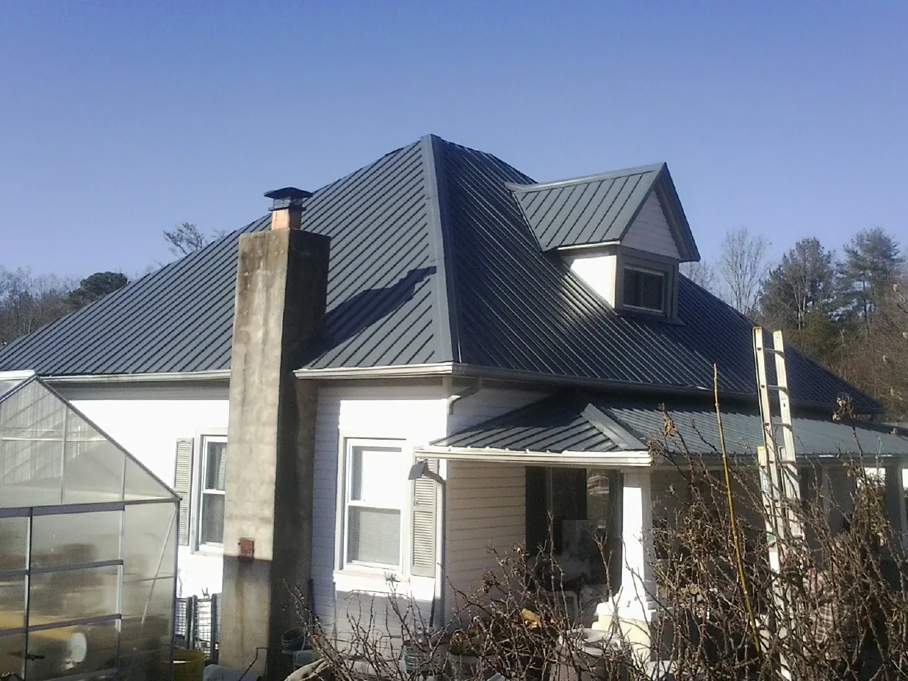 Dark blue standing seam metal roof on a white farmhouse with dormer — Slate & Tile Roof Repair by Roofing Brothers in Toano