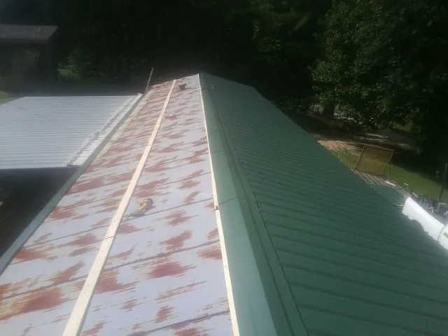 Old rusted panels beside newly installed green metal roofing — Wind Damage Roof Repair by Roofing Brothers in Toano