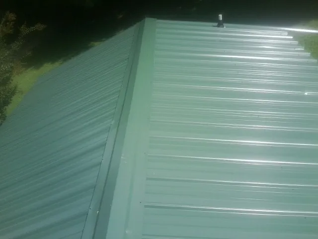 New green metal panels meeting at the ridge of a roof — Flat Roof Repair work by our crew in Toano