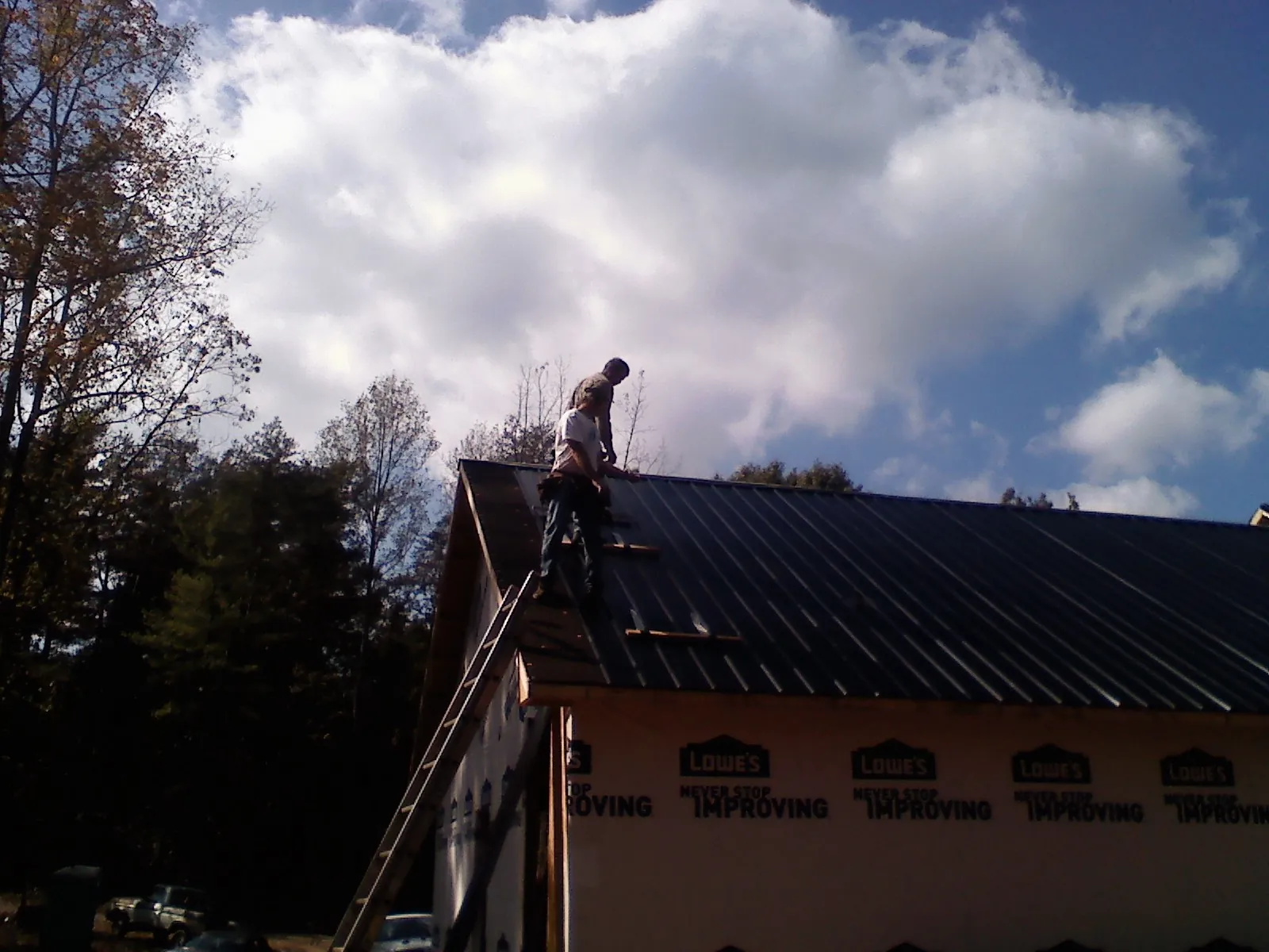 Roofer fastening dark metal panels high against a cloudy sky, from a Roof Inspection job in Toano
