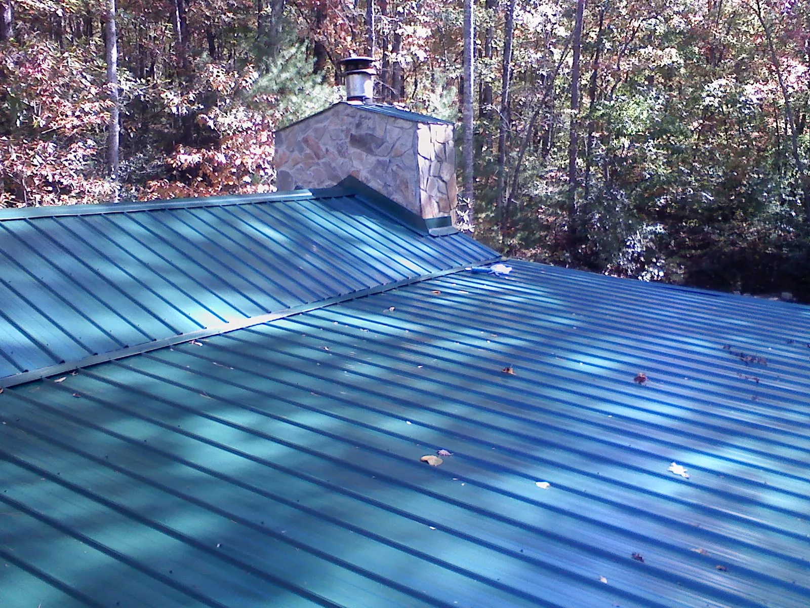 New green metal roof and stone chimney surrounded by autumn woods in Toano