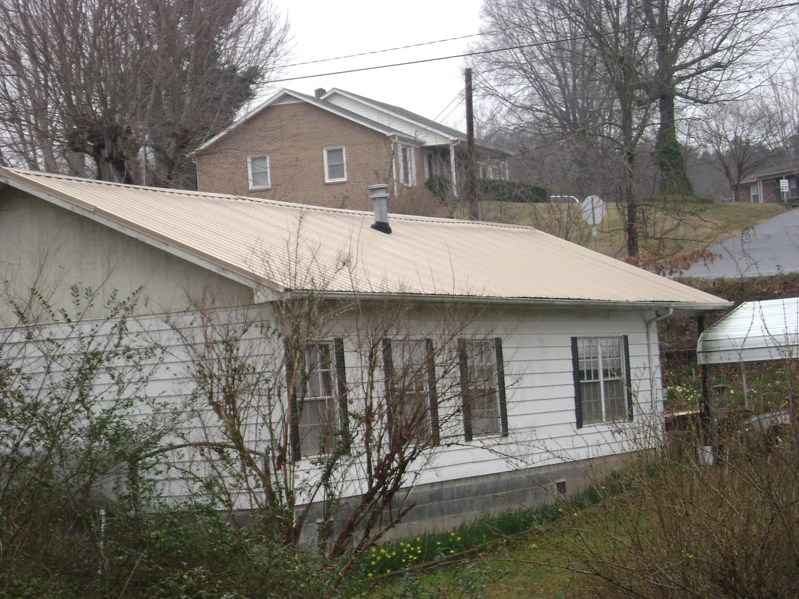 Tan metal roof on a white sided house set into a hillside — Commercial Roofing by Roofing Brothers in Toano